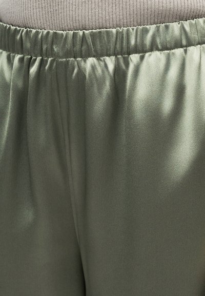 Κοντινή λήψη παντελονιών από σατέν ελιάς με ελαστική μέση με σούρες και ανοιχτό μπεζ πάνω άκρο που φαίνεται πάνω από τη μέση.