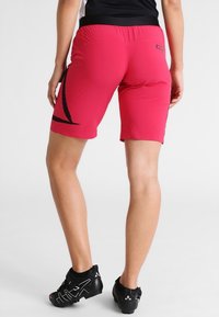 Red athletic shorts with a black design accent, featuring a stretchy waistband and flat seams for comfort. Worn with black cycling shoes.