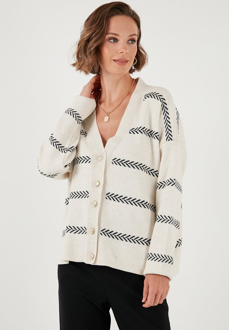 Cardigan crema con rayas de espiga negras, escote en V y cinco botones. Textura suave con mangas largas y corte relajado.