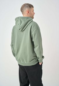 Green hoodie with a drawstring hood and kangaroo pocket, made from a soft fabric. The back shows a relaxed fit with ribbed cuffs and hem.