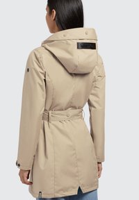 Beige waterproof jacket with a hood, belted waist, and button accents. Smooth texture, mid-length design, and logo patch at the back.