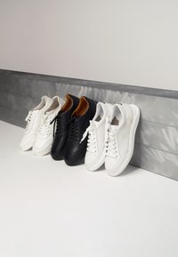 Trzy pary sneakersów: jedna biała ze skóry, jedna czarna ze skóry i jedna biała z siateczki z skórzanymi akcentami. Każda z nich ma sznurówki i zaokrąglony czubek.