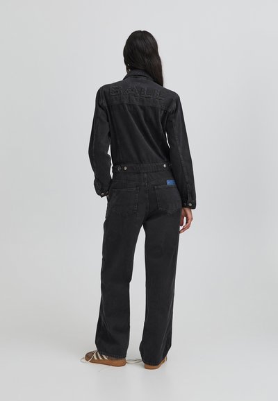 Melnas džinsa kombinezons ar garām piedurknēm, priekšējo pogu aizdari un izspiestu "Balle" logo aizmugurē. Tam ir brīva piegriezuma forma un divas aizmugurējās kabatas.