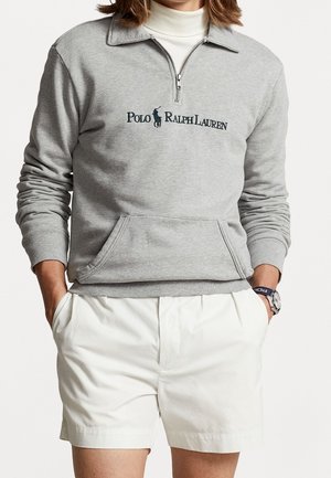 Gray cotton pullover with a half-zip collar, featuring an embroidered logo and a front pocket. Paired with white shorts.