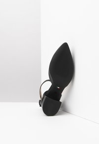 Scarpa nera con tacco alto e punta affilata, dotata di una suola texturizzata e di un sottile cinturino per la caviglia. Made in Italy.