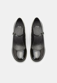 Black patent leather Mary Jane shoes with a rounded toe and a decorative strap featuring a silver-tone buckle. Smooth texture, flat sole.