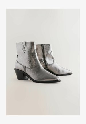 Metalické stříbrné kotníkové boty s špičatou špičkou, texturovanou kůží, zkosenými stranami a černým nízkým podpatkem. Zapínání na zip na zadní straně.