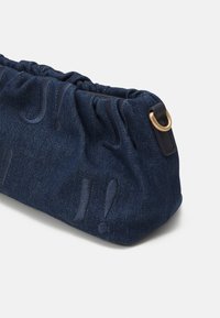 Sacoche en denim bleu foncé avec un design de haut froncé. Comprend des points d'exclamation embossés et un accent en anneau métallique doré. Tissu texturé.