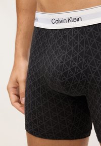 Fekete boxer alsónadrág gyémántmintával és fehér Calvin Klein elasztikus derékpánttal, lapos varrásokkal és feszes illeszkedéssel.