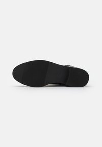 Černá podrážka boty s hladkým, texturovaným povrchem a horizontálními drážkami pro lepší přilnavost. Materiál se zdá být guma a má minimalistický design.