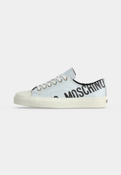 Baskets basses blanches avec œillets argentés, lacets blancs et texte noir "MOSCHINO" sur le côté et le talon sur fond blanc.