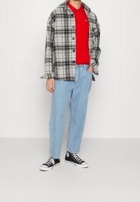 Červený polo tričko pod černobílou kostkovanou košilí, světle modré volné džíny a černé nízké tenisky. Jednoduchý design, volný střih.