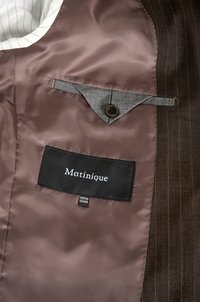 De binnenkant van het bruine gestreepte colbert heeft een glanzende bruine voering, grijze zakdetails en een zwart label met "Matinique" en maatinformatie.