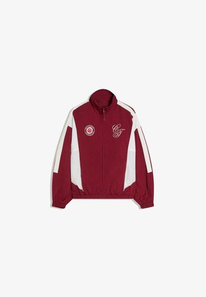 Bordó és fehér cipzáras dzseki rugalmas mandzsettákkal, magas gallérral, "C&T" felirattal a mellkasnál, és egy kör alakú, rózsát ábrázoló logóval a bal oldalon.