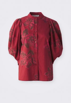 Blouse bordeaux avec un col rond, un devant boutonné et des manches bouffantes. Présente un motif floral dans des teintes plus foncées et une texture en coton doux.