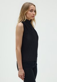 Zwarte mouwloze top met een opstaande kraag, voorzien van een verticale ribbelstructuur en een aansluitende silhouet, gecombineerd met zwarte broek.