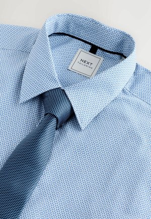 Blau gemustertes Hemd mit scharfem Kragen und einer passenden dunkelblauen strukturierten Krawatte, die ein kleines Etikett mit "NEXT TAILORING" trägt.