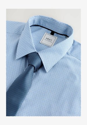 Blau gemustertes Hemd mit scharfem Kragen und einer passenden dunkelblauen strukturierten Krawatte, die ein kleines Etikett mit "NEXT TAILORING" trägt.
