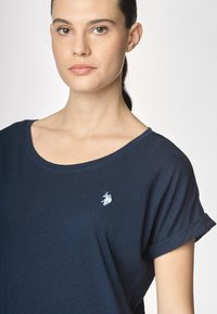 T-shirt blu navy realizzato in morbido cotone con vestibilità rilassata, dotato di maniche corte arrotolate e un piccolo logo ricamato sul petto.