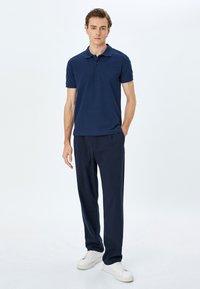 Marinblå polo t-shirt med krage, korta ärmar och en texturerad mönster, kombinerad med mörk marinblå byxor och vita sneakers.