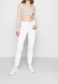 Beige dlouhý rukáv zkrácený top s předními knoflíky, který je spárovaný s bílými vytáhlými džínami s vysokým pasem a bílými teniskami. Jednoduchý a moderní design.