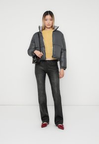 Grå kort puffjakke med leopardmønsterfôr, gul ullgenser, svarte jeans og røde sko, mot en hvit bakgrunn.