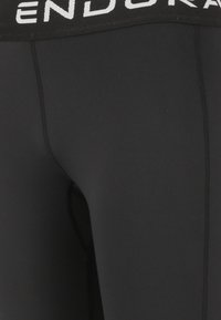 Schwarze Leggings mit einem breiten, elastischen Bündchen, auf dem "ENDURA" in Weiß steht. Der Stoff ist glatt, hat eine taillierte Passform und keine sichtbaren Muster.