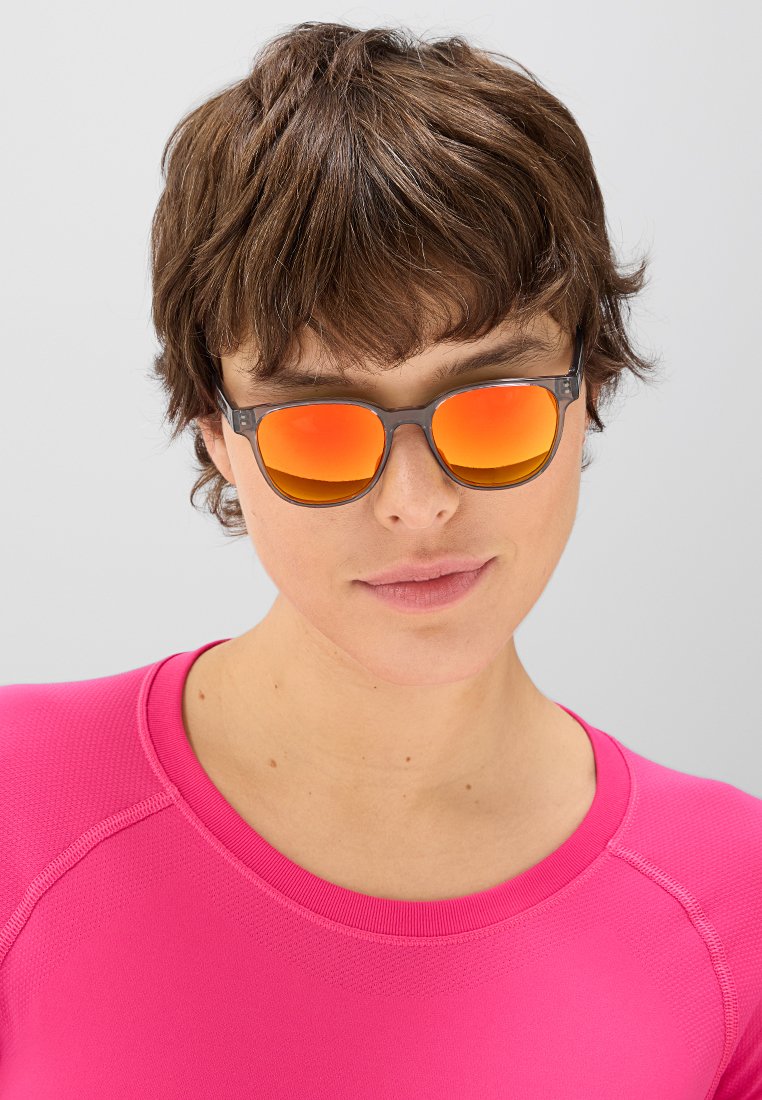 Okulary przeciwsłoneczne z szarymi oprawkami i pomarańczowymi lustrzanymi soczewkami. Noszone z dopasowaną różową koszulą, podkreślając nowoczesny design i elegancki kontrast kolorów.