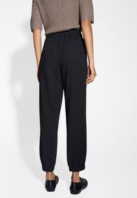 Pantaloni neri con vita elasticizzata e caviglie a polsino, dotati di due tasche posteriori, realizzati in tessuto liscio. La forma aderente migliora il comfort e il movimento.