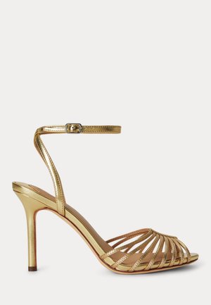 Sandale à talons hauts dorée avec plusieurs fines lanières et une bride avec boucle à la cheville, présentée de profil sur fond blanc.