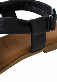 Schwarze Ledersandale mit breitem Riemen, schlankem Design, braun gepolstertem Fußbett und flacher Sohle. Verfügt über einen verstellbaren Schnallenverschluss und minimalistische Nähte.