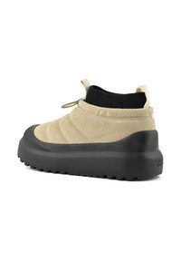 Beige semišové kluše s černým polstrovaným kotníkovým lemem, silnou černou podrážkou a zdrhovadly na patě a jazyku na bílém pozadí.