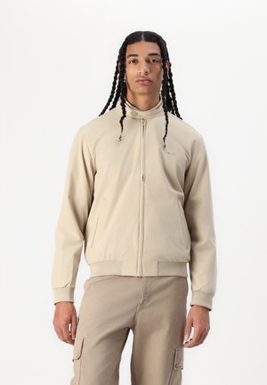 Beige bomber jacket with a high collar, front zipper, and elastic cuffs. Features side pockets and smooth, lightweight fabric.