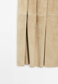 Gonna in suede beige con una consistenza morbida, caratterizzata da due pieghe verticali e una finitura liscia. Ha un design fino al ginocchio e linee pulite.