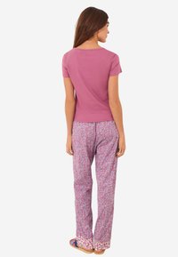 Enganliegendes pinkes Kurzarmoberteil kombiniert mit gemusterten, pink-weißen weit geschnittenen Hosen mit floralem Design. Einfache flache Sandalen runden das Outfit ab.