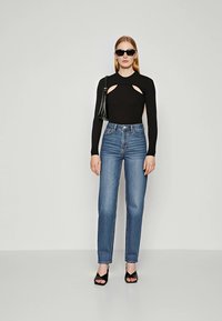 Μαύρο μπλουζάκι με μακριά μανίκια και λεπτομέρειες κοπής, σε συνδ�υασμό με ψηλόμεσα μπλε τζιν, μαύρα γυαλιά ηλίου και μαύρες ψηλές σάντες. Μινιμαλιστικός σχεδιασμός.