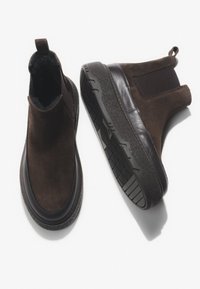 Brązowe zamszowe botki za kostkę z gładkim paskiem ze skóry, elastycznymi panelami bocznymi oraz teksturowaną gumową podeszwą zapewniającą przyczepność i stabilność.