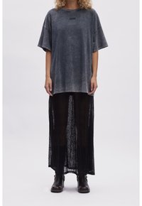 Grå oversized t-shirt med korte ærmer og et subtilt print, parret med en lang sort gennemsigtig nederdel. Sorte ankelstøvler fuldender outfittet.