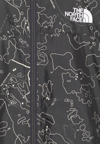 Detailní záběr na černou bundu s potiskem bílé konturové mapy a viditelným zipem, která má logo The North Face v pravém horním rohu.