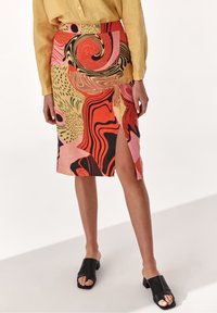 Falda de talle alto con patrones multicolores vibrantes, que presenta remolinos y acentos en rojo, rosa y amarillo, con una abertura lateral.
