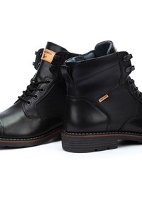 Botas de tobillo de cuero negro con paneles de malla, punta redonda y suelas de goma. Presentan costuras en contraste y una etiqueta de cuero con la marca.