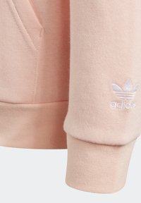 Felpa rosa con una texture morbida, maniche a costine e un logo ricamato bianco sulla manica. Include una tasca laterale per il deposito.