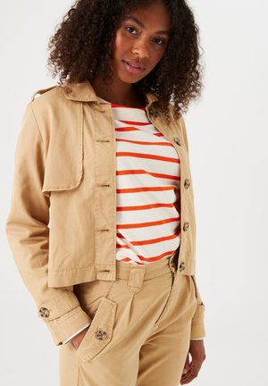 Beige cropped jas met knoopdetails, gestyled met een gestreept rood-wit top. Opvallende zakken en manchetontwerp; gladde stofstructuur.
