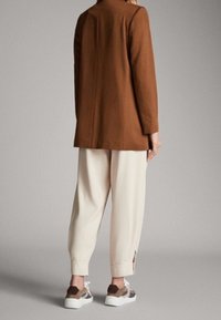 Brązowy blezer z długim rękawem, kremowe zwężane spodnie z bocznymi rozcięciami oraz wielokolorowe sneakersy. Gładka tkanina o dopasowanym kroju i czystych liniach.