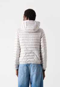 Zilveren pufferjack met capuchon, voorzien van doorgestikte lijnen, elastische manchetten en een slim fit. Draag het met lichtblauwe spijkerbroek.