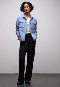 Jasnoniebieska teksturowana kurtka z dwoma przednimi kieszeniami, zapięciem na guziki, noszona na białej koszuli i czarnych spodniach, uzupełniona czarnymi butami.