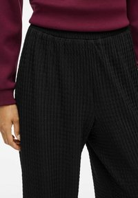 Pantalons noirs texturés avec un motif en zigzag, dotés d'une taille élastique et d'une coupe décontractée. Associés à un sweat-shirt bordeaux.