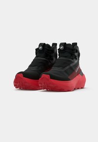 Zwarte en rode wandelschoenen met een gestructureerde stoffen bovenkant, rubberen zool en versterkte neuskap. Voorzien van trekbanden en logo-accenten.