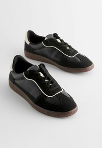 Sneakers neri con un mix di camoscio e pelle, con una finitura testurizzata, accenti bianchi e una suola in gomma marrone. Design con lacci.