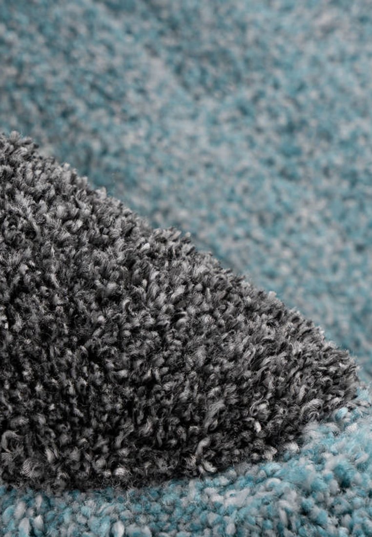 Strukturierten, plüschigen Teppich mit einer Mischung aus grauen und blauen Fasern, der eine weiche, strohige Oberfläche und kontrastierende Farbbereiche aufweist.